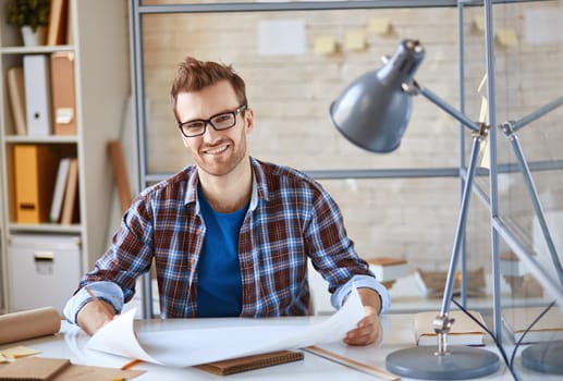 Young businessman with blueprint looking at camera at workplace