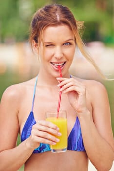 Happy female in bikini drinking orange juice and winking