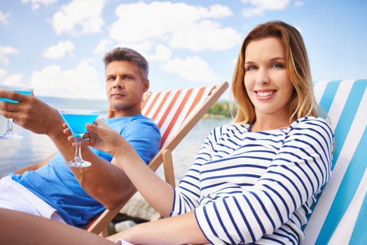 Young woman and man with cocktails sitting on deckchairs and looking at camera