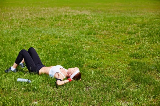 Young woman in activewear relaxing on green lawn