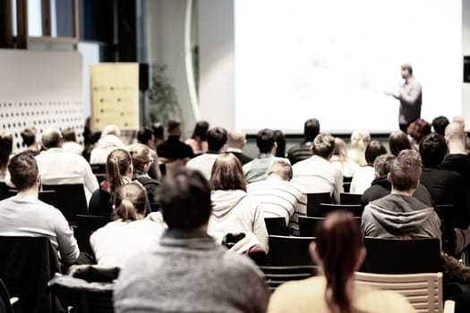 Speaker giving a talk in conference hall at business event. Audience at the conference hall. Business and Entrepreneurship concept. Focus on unrecognizable people in audience.