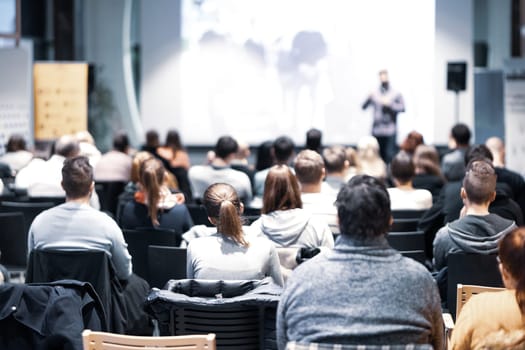 Speaker giving a talk in conference hall at business event. Rear view of unrecognizable people in audience at the conference hall. Business and entrepreneurship concept.