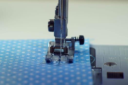 Detailed close up shot of sewing machine steel foot with needle and thread stitching on blue fabric polka dot textile. Sewing machine, tailor's shop, atelier, dressmaker industry. Needle craft