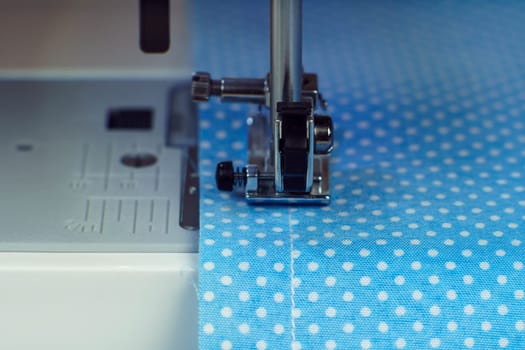 Close up sewing machine steel part with needle, pressure foot stitching with thread on blue fabric, textile. Dressmaker or tailoring industry, workshop and atelier. Needle craft and manufacture work