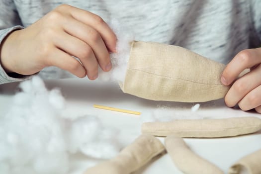 Unrecognizable closeup of woman designer hands sewing soft toys. Create paws and body part, stuffed them with cotton on table. Kid present shop, store. Small business, creative occupation and tutorial