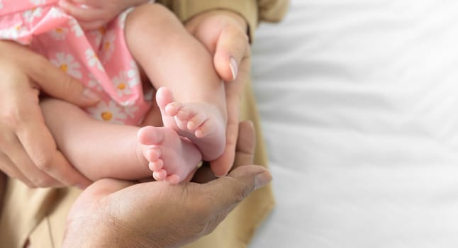 Father and mother hands holding newborn baby feet. Feet of newborn on the palms of parents. Family parents love concept