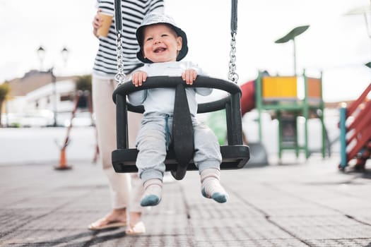 Mother pushing her infant baby boy child on a swing on playground outdoors