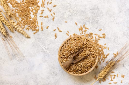 Bowl of raw dry rye grain with a wooden spoon on white table top view. Healthy alternative low gluten seeds. Protein source for vegan and vegetarian diet.