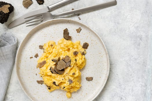 Scrambled eggs with sliced fresh black truffles from Italy served in a plate near fork and knife top view. Italian cousine, gourmet breakfast