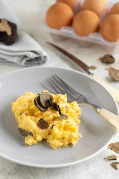 Scrambled eggs with sliced fresh black truffles from Italy served in a plate near fork and knife close up. Italian cousine, gourmet breakfast