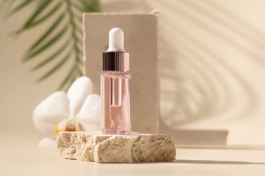 Dropper Bottle on stone near white orchid flowers with palm leaf on beige, close up. Skincare beauty product, essential oil or serum. Exotic cosmetics, pastel minimal composition..