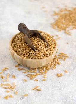 Bowl of raw dry rye grain with a wooden spoon on white table close up. Healthy alternative low gluten seeds. Protein source for vegan and vegetarian diet.