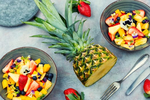 Fresh salad of pineapple, strawberries and berries, decorated with edible flowers.Copy space.