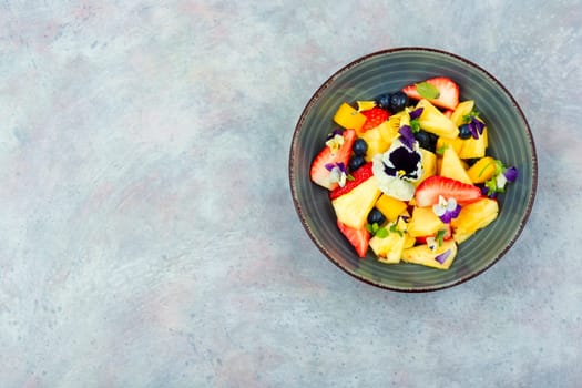 Fresh salad of pineapple, strawberries and berries, decorated with edible flowers.Copy space.