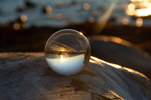 Glass ball on a rock at sunset on the beach, the sea and the setting sun are reflected in the ball