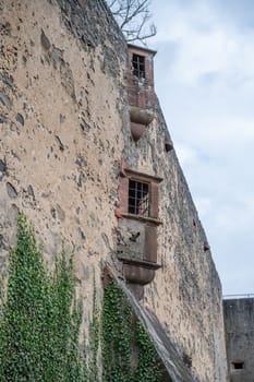 Balcony with metal grid windows and Ronneburg Castle during cloudy day, view from low angle, Germany, vertical shot