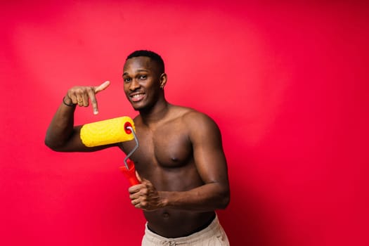 African painter focused on work holding professional roller to paint interior wall, studio.