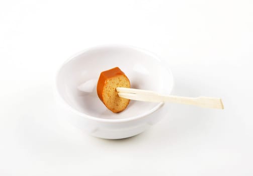 Slice of tofu sausage on wooden skewer in porcelain bowl on white background