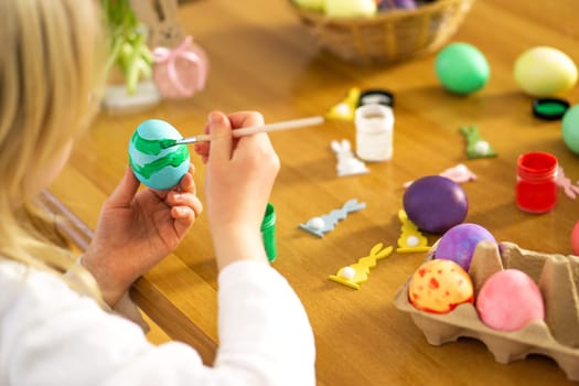 Little child hands painting colored Easter eggs on the wooden table at home. Happy Easter. Preparation for Easter celebration.