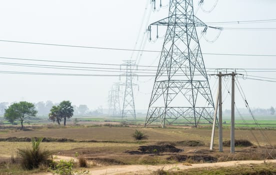 Power lines over an agricultural field against clear sky horizon. High-voltage tower installed in a row on a field.