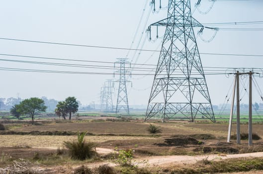 Power lines over an agricultural field against clear sky horizon. High-voltage tower installed in a row on a field.