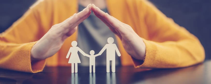 Woman holding her hands in the form of a roof over the figurines of a family.Concept of the care and security in relation.