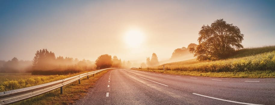 Sunrise in the foggy morning on the empty asphalt country winding road. Curve street in natural park.