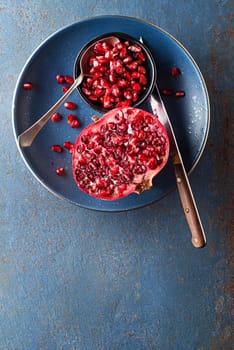 Healthy ripe pomegranate fruit opened and splitted with seeds in cup on blue background