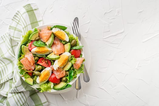 Fresh green lettuce salad with smoked salmon, cherry tomatoes, egg and avocado on white table background