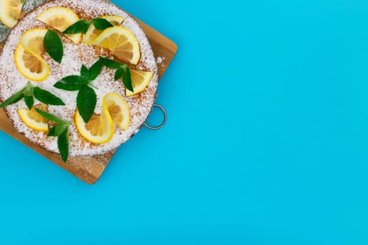 Lemon pie with lemon slices, mint and powdered sugar on a blue background. Top view, copy space.