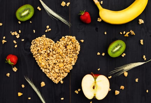 Heart laid out of granola, fruits and spikelets on a black wooden background. Flat lay.