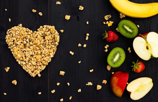 Heart laid out of granola and fruits on a black wooden background. Flat lay. Copy space.