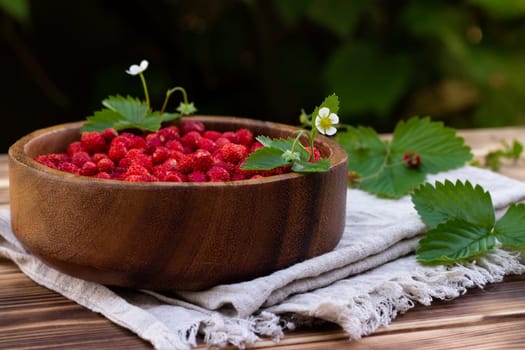 A wooden bowl of red ripe wild strawberries and flowers on an old wooden surface.