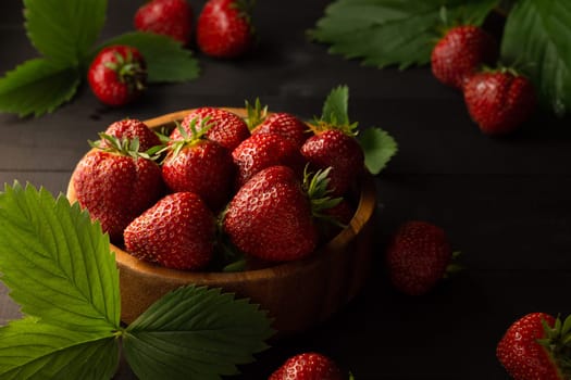 A wooden bowl of fresh red ripe strawberries on a black wooden surface. Low key. Copy space.