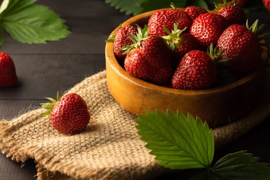 A wooden bowl of fresh red ripe strawberries on a black wooden surface. Low key. Copy space.