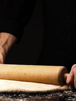 Baker or cook rolls out an organic yeast dough on the work surface, black background with space for your text or image, traditional handwork in the kitchen