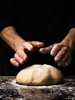 Baker or cook kneads an organic yeast dough, black background with space for your text or image, traditional handwork in the kitchen