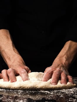 Baker or cook kneads an organic yeast dough, black background with space for your text or image, traditional handwork in the kitchen