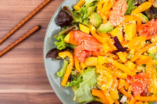 Tasty salad with salmon, mango, sesame avocado and pepper. Healthy eating, space for text. Food and chopsticks