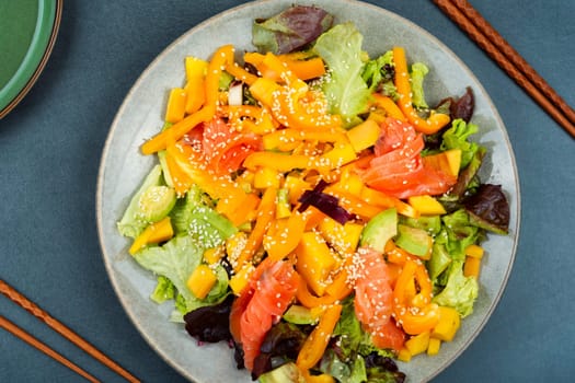 Tasty salad with salmon, mango, sesame avocado and pepper. Healthy eating, space for text. Food and chopsticks