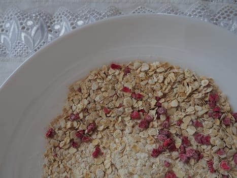 Organic Granola Cereal with oats, powdered sugar and dry raspberries. Healthy muesli as a dry mix. An antidiabetic, low calorie, healthy diet. White utensils.