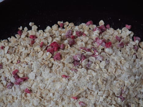 Organic Granola Cereal with oats, powdered sugar and dry raspberries. Healthy muesli as a dry mix. An antidiabetic, low calorie, healthy diet. Black utensils.
