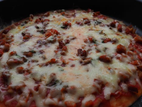 whole pizza close up. Delicious, juicy round pizza with tomatoes, salami. The melted cheese pours over the surface of the baked cake. Counter light. Soft blurred focus.