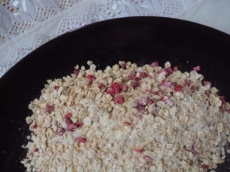 Organic Granola Cereal with oats, powdered sugar and dry raspberries. Healthy muesli as a dry mix. An antidiabetic, low calorie, healthy diet. Black utensils.