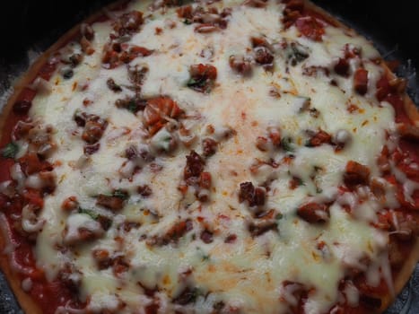 whole pizza close up. Delicious, juicy round pizza with tomatoes, salami. The melted cheese pours over the surface of the baked cake. Counter light. Soft blurred focus.