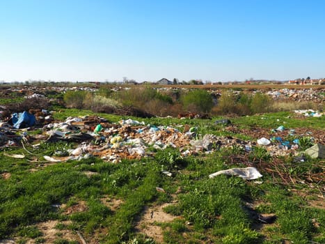 garbage dump near the village. Chaotic unofficial dump. Plastic, bags, paper, glass, biological waste. Green grass next to dirt. Ecological catastrophy