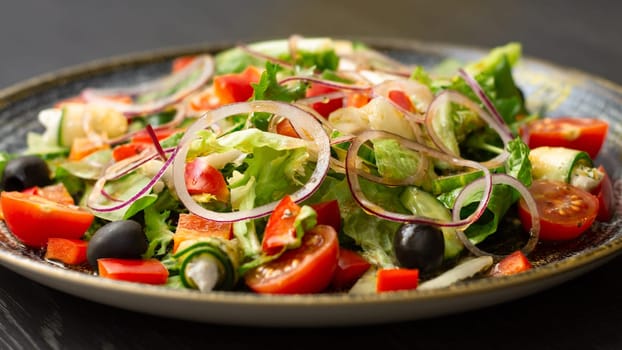 Vegetable salad with greens and olives in dark clay plate on wooden table