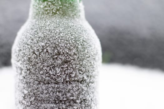 Partially blurred bottle of beer covered with hoarfrost in snow on dark background, copy space