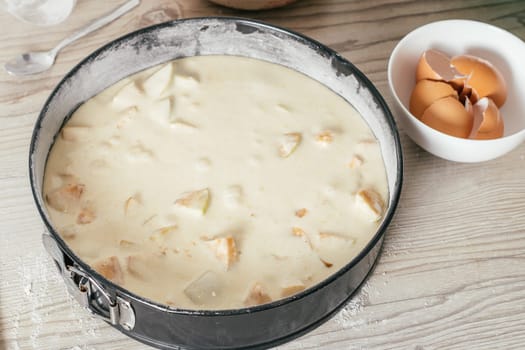 Baking dish with raw apple pie dough stands on kitchen counter, next to bowl with eggshells