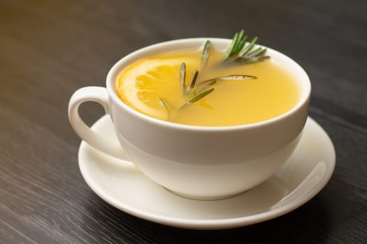 Yellow ginger tea with lemon and rosemary branch in white cup on wooden table
